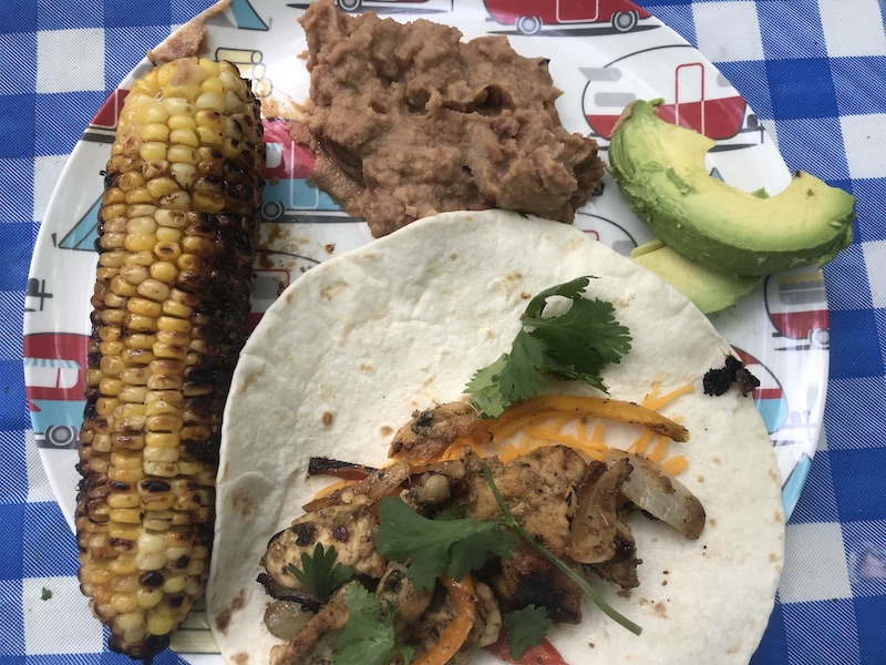 grilled chicken fajitas on a plate with corn, refried beans and avocado